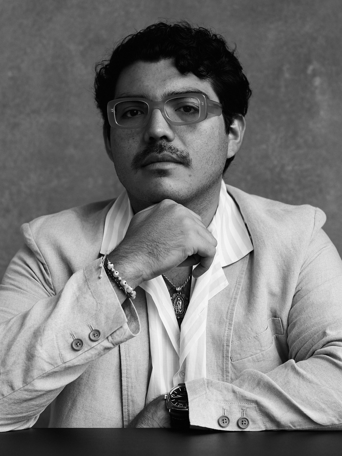 Black-and-white portrait of Salomón Flamenco in a light blazer and striped shirt, chin resting on his hand